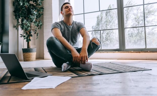 relaxed student sits crossed legs on floor near opened laptop