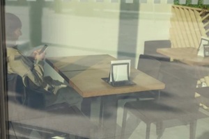 person is casually sitting at a dining table within a bustling restaurant, focused intently on their smartphone device in front of them